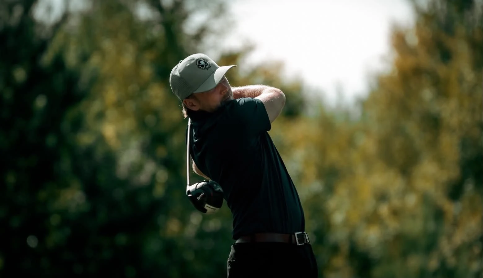 Golfare i Swinghard-piké i avslutad sving, med grönska i bakgrunden